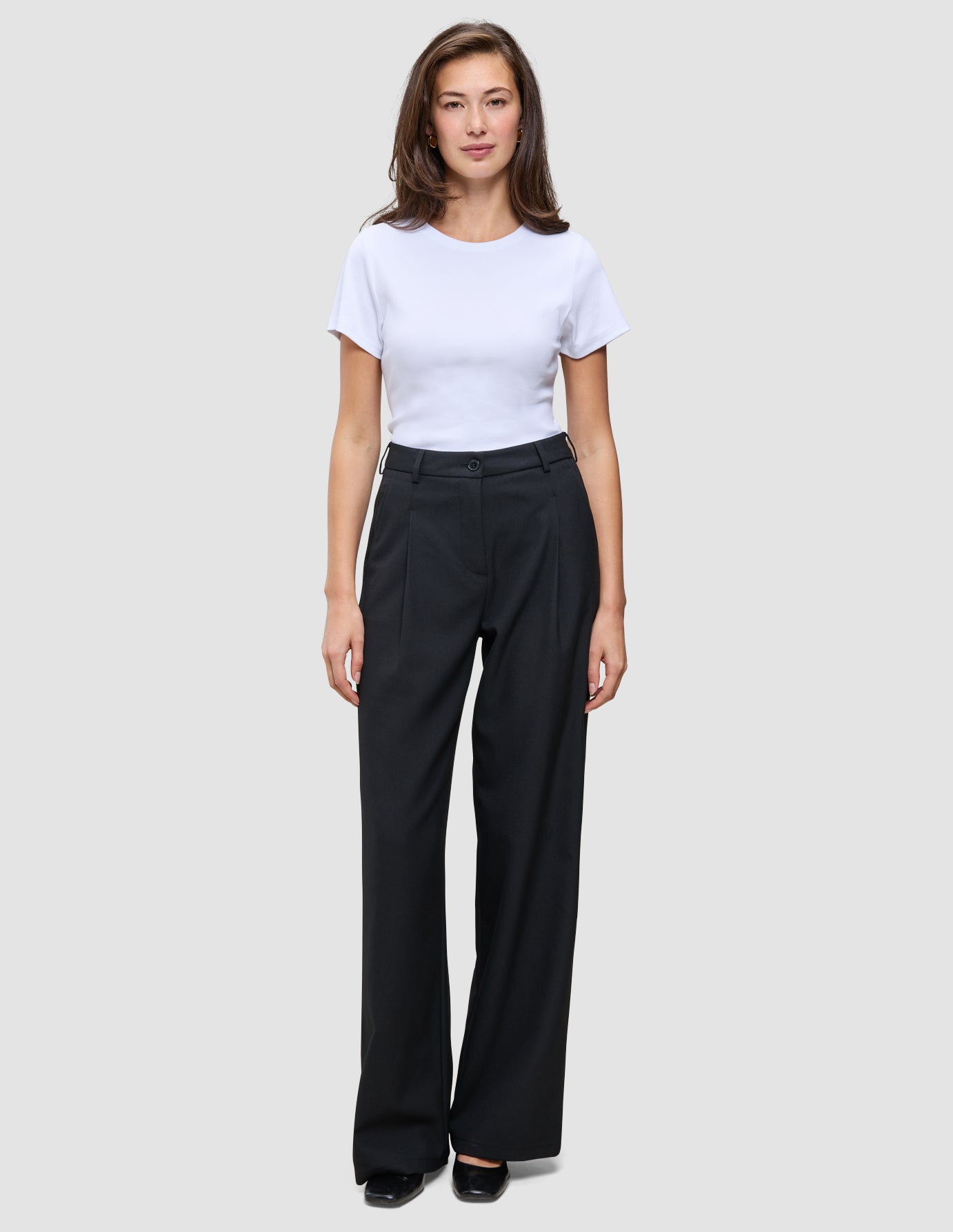 En kvinde iført en hvid T-shirt og et par Serene Pants Wide Black med brede ben.